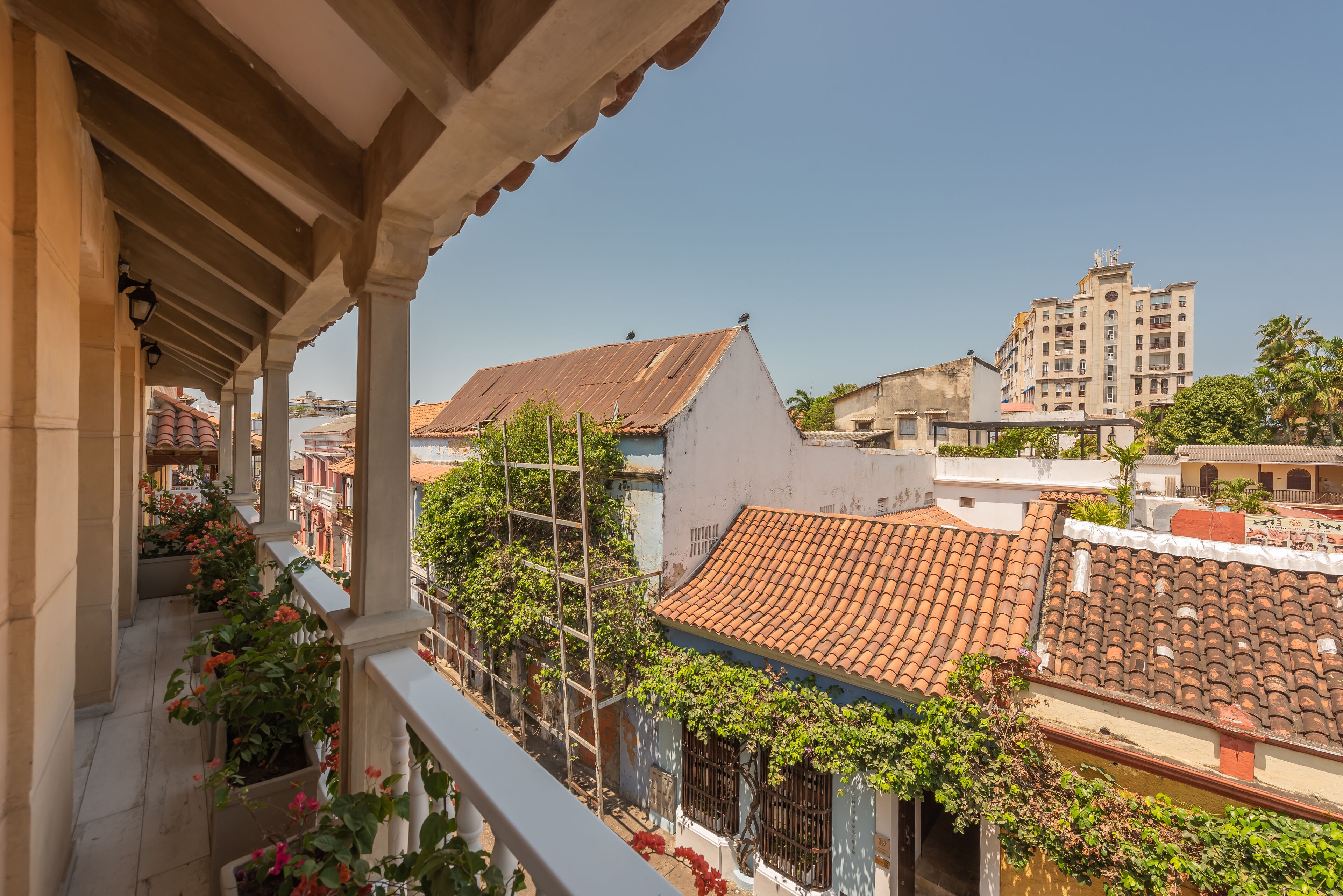 A balcony with a view of terracotta-tiled buildings, a pergola, and climbing plants.