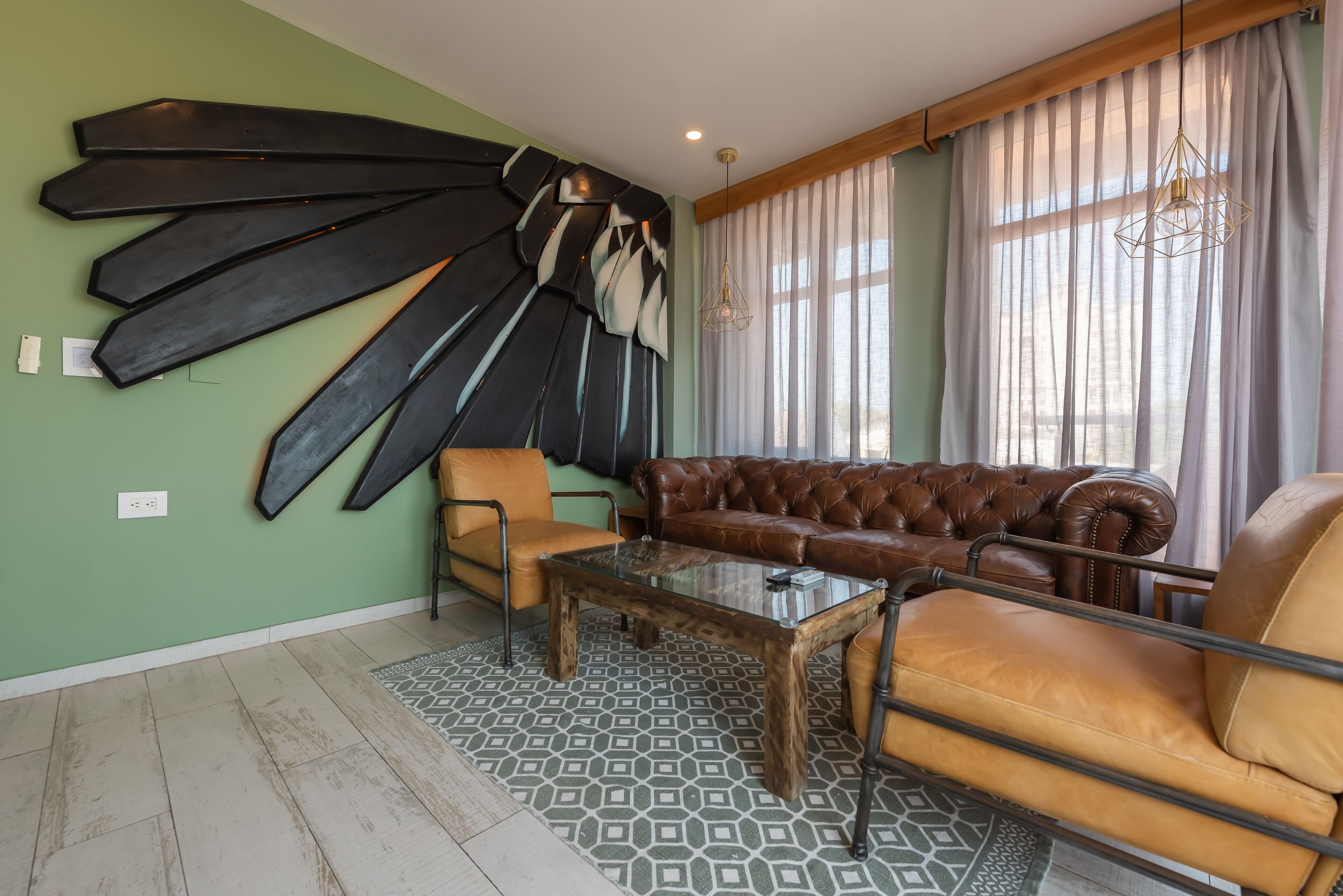Una sala de estar con un sofá de cuero marrón, una mesa de centro de vidrio y una alfombra estampada.