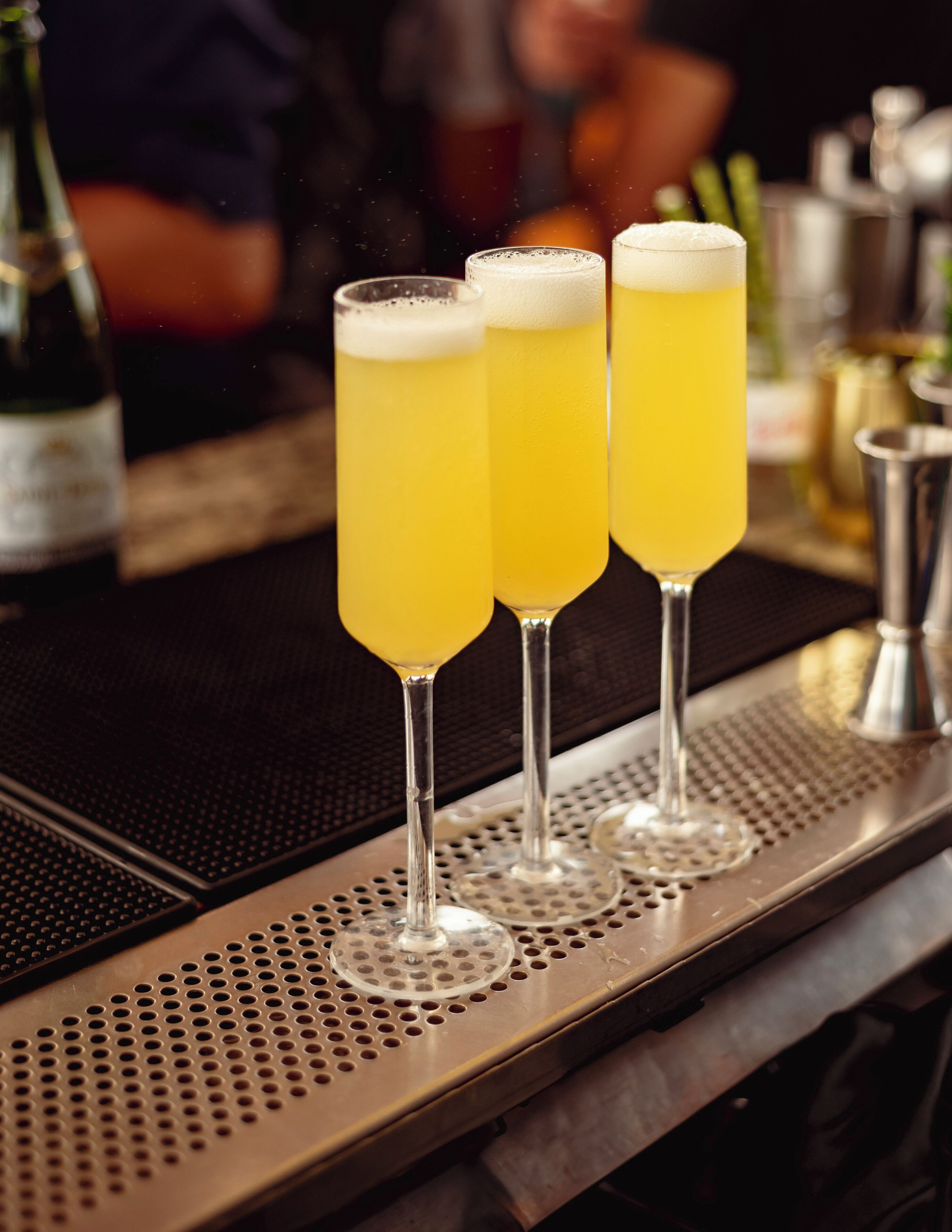 Three glasses of yellow beverage on a bar mat.