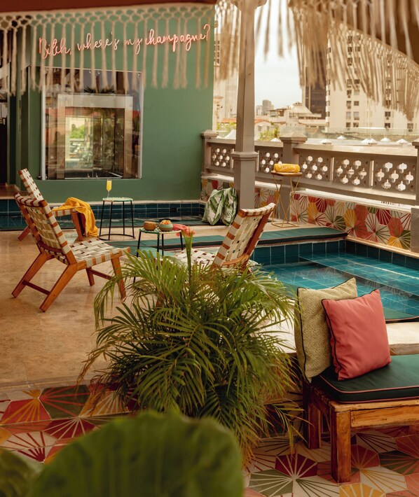 A poolside area with lounge chairs, a small table with a drink, and a neon sign.