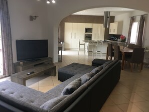 Ein modernes Wohnzimmer mit einem grauen Sofa, einem Fernseher und einem Essbereich mit Stühlen und einem Tisch.