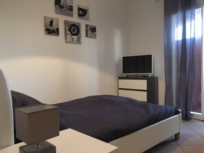 Ein Schlafzimmer mit einem Bett, einem Nachttisch mit Lampe, einem Fernseher auf einem Schrank und Kunstwerken an der Wand.
