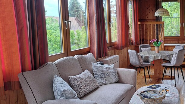 Una habitación acogedora con sofá, una mesa de comedor con sillas y ventanas grandes con cortinas.