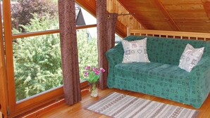 Una cabaña de madera acogedora con un sofá verde estampado, una ventana con cortinas y vistas a árboles.