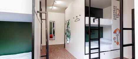 A dormitory room with bunk beds, a green wall, a mirror, a wall-mounted towel rack, and a motivational quote.