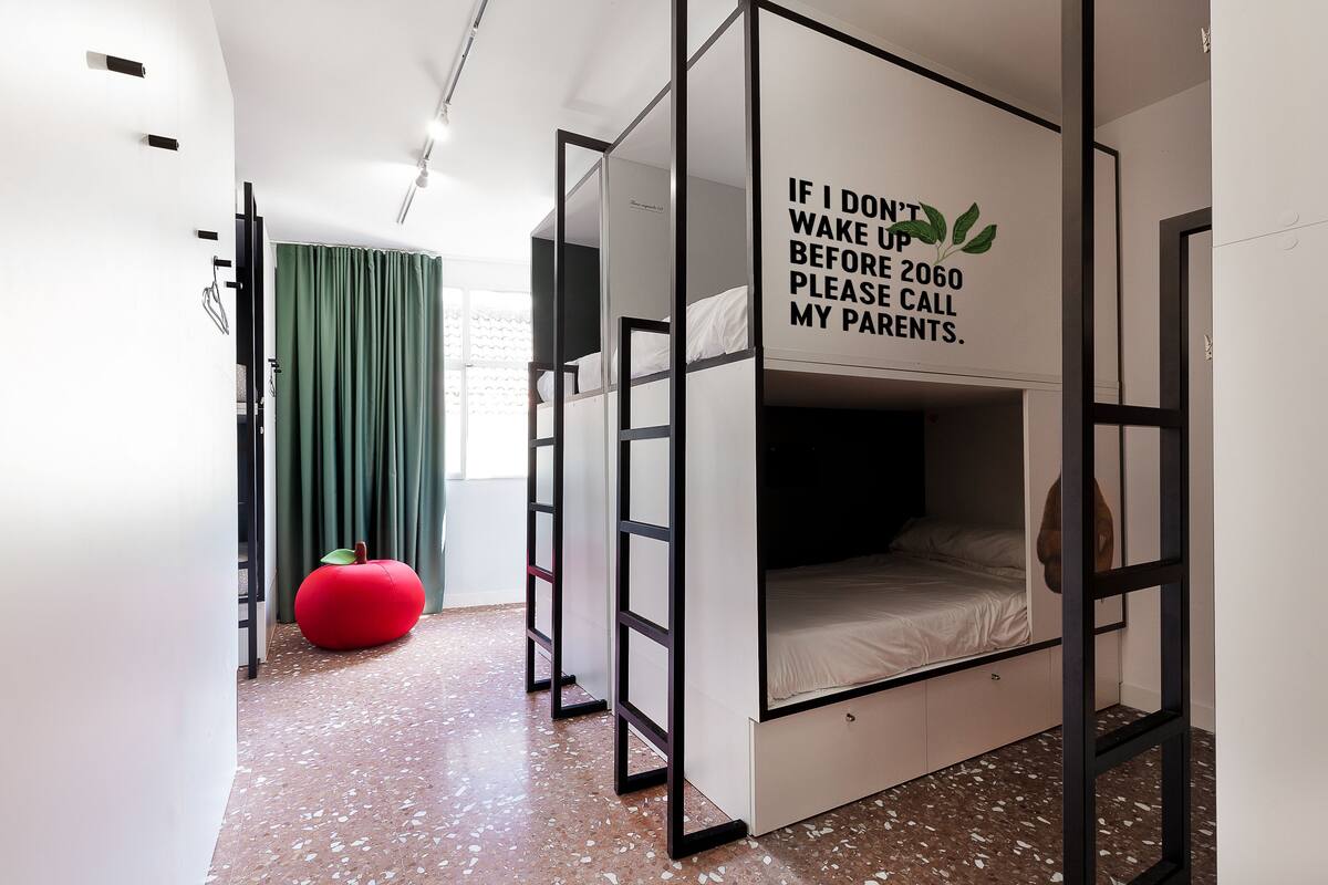 A modern room with a bunk bed, a red bean bag, and a wall with a humorous message.