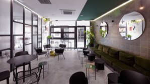 Un interno moderno con un divano verde, tavolini e sedie rotonde, ampie finestre e una parete verde a contrasto.