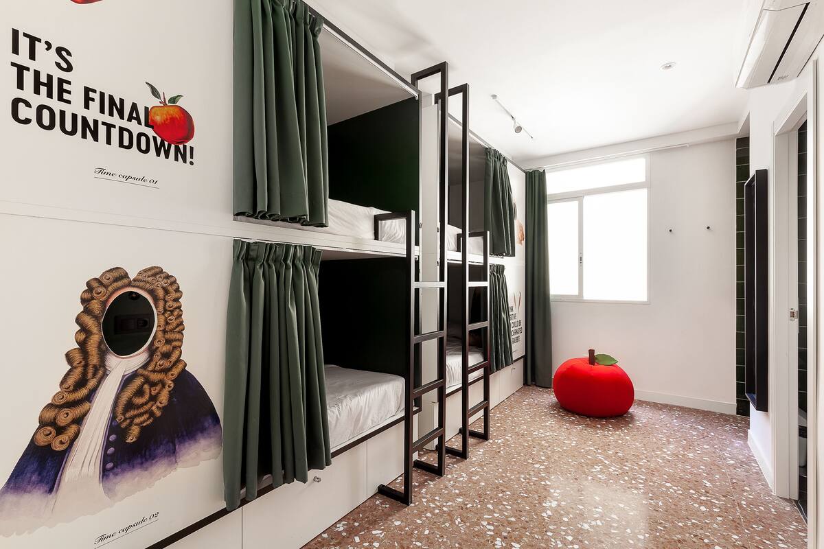 A bunk bed room with a large poster, a red apple-shaped cushion, and a window.