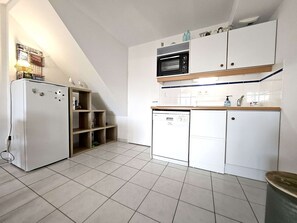 Eine kleine Küche mit Kühlschrank, Mikrowelle und Geschirrspüler, Holzregalen und Fliesenboden.