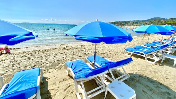 Uma praia com fileiras de cadeiras de praia brancas e guarda-sóis azuis.