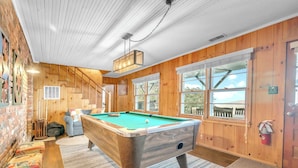 Une table de billard dans une pièce aux murs en bois et aux grandes fenêtres.
