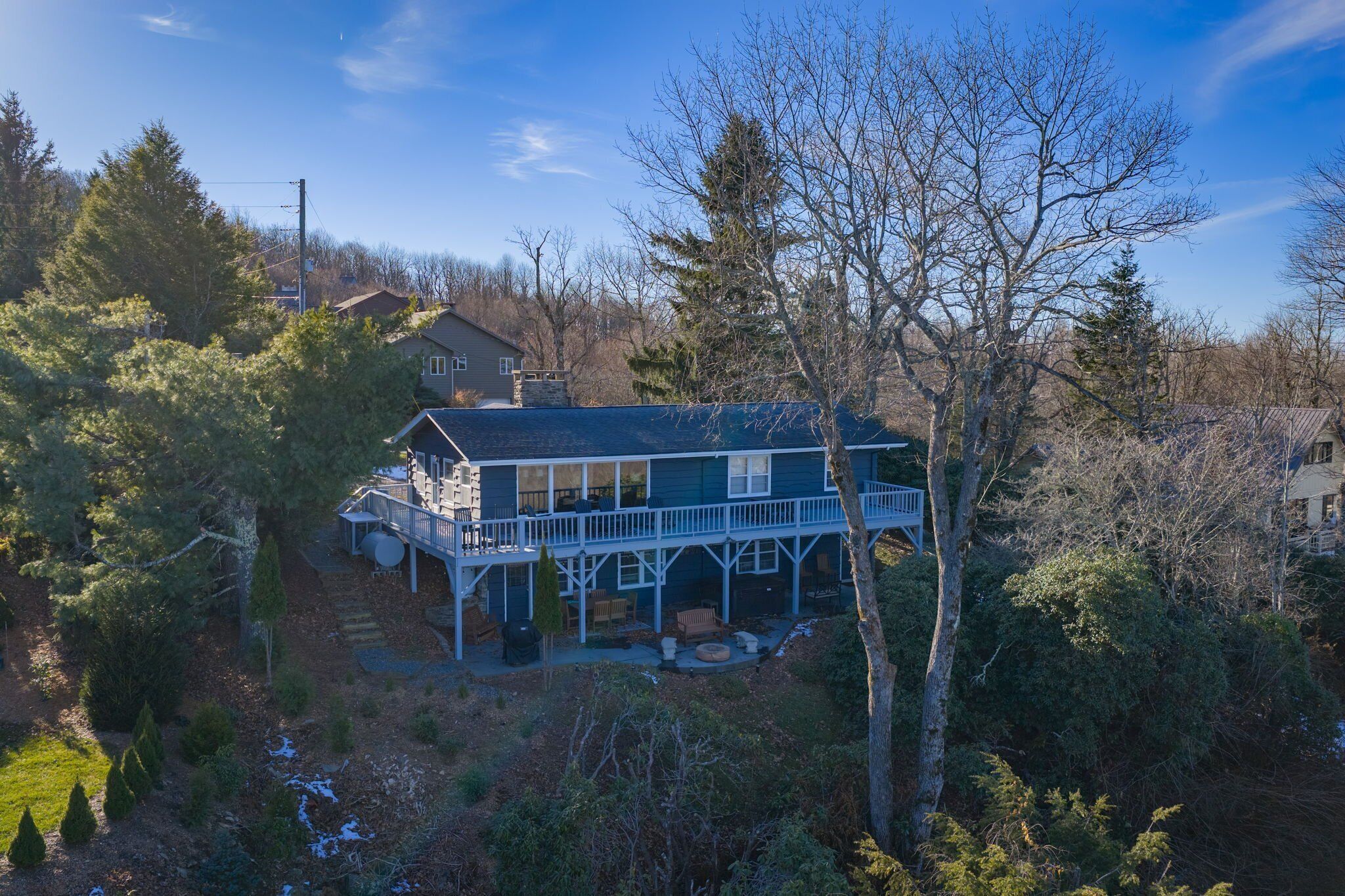 Une maison à deux étages, dotée d’un balcon et d’un porche abrité, entourée d’arbres et sous un ciel dégagé.