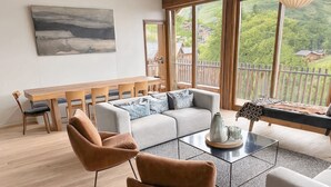 A spacious room with a wooden ceiling, large windows, a sofa, a coffee table, and a dining area.