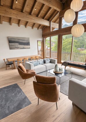 En rummelig stue med trælofter, store vinduer, en sofa, et sofabord og et spiseområde.
