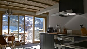 A modern kitchen with a large window, wooden ceiling, and a view of a snowy landscape.