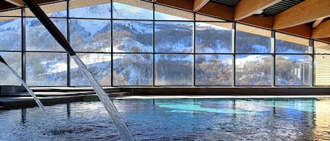 Une piscine intérieure avec vue sur les montagnes enneigées, grâce à de grandes fenêtres.