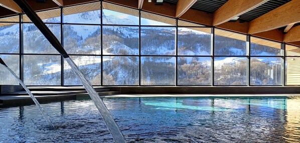 En indendørs swimmingpool med udsigt til sneklædte bjerge gennem store vinduer.