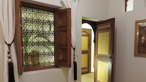 A hallway with a window featuring ornate metalwork and a wooden door with intricate patterns. - Riad "LA DOUIRIA" in exclusivity (Marrakech)