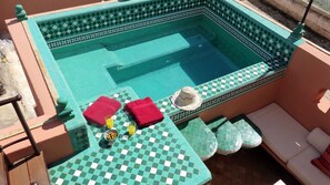 A pool area with checkered tiles, a lounge chair, a small table with a drink and snacks, and a hat on the table. - Riad "LA DOUIRIA" in exclusivity (Marrakech)