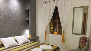 A hotel room with a bed, a chair, a window with curtains, a mirror, and a decorative wall. - Riad "LA DOUIRIA" in exclusivity (Marrakech)