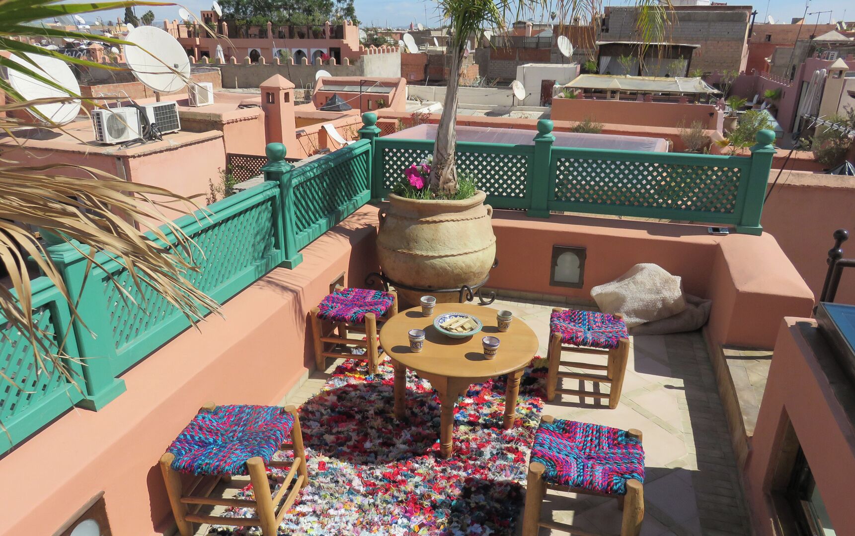 A rooftop terrace with a table and chairs, a large potted plant, and a view of surrounding buildings.