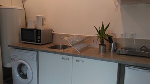A compact kitchen with a washing machine, microwave, and a drying rack. - 2* furnished studio - La Maison aux Mille Roses (Nieul-Sur-Mer)