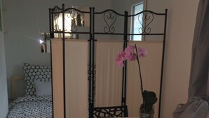 A room with a bed, a dining table with chairs, a partition, and a hanging orchid. - 2* furnished studio - La Maison aux Mille Roses (Nieul-Sur-Mer)