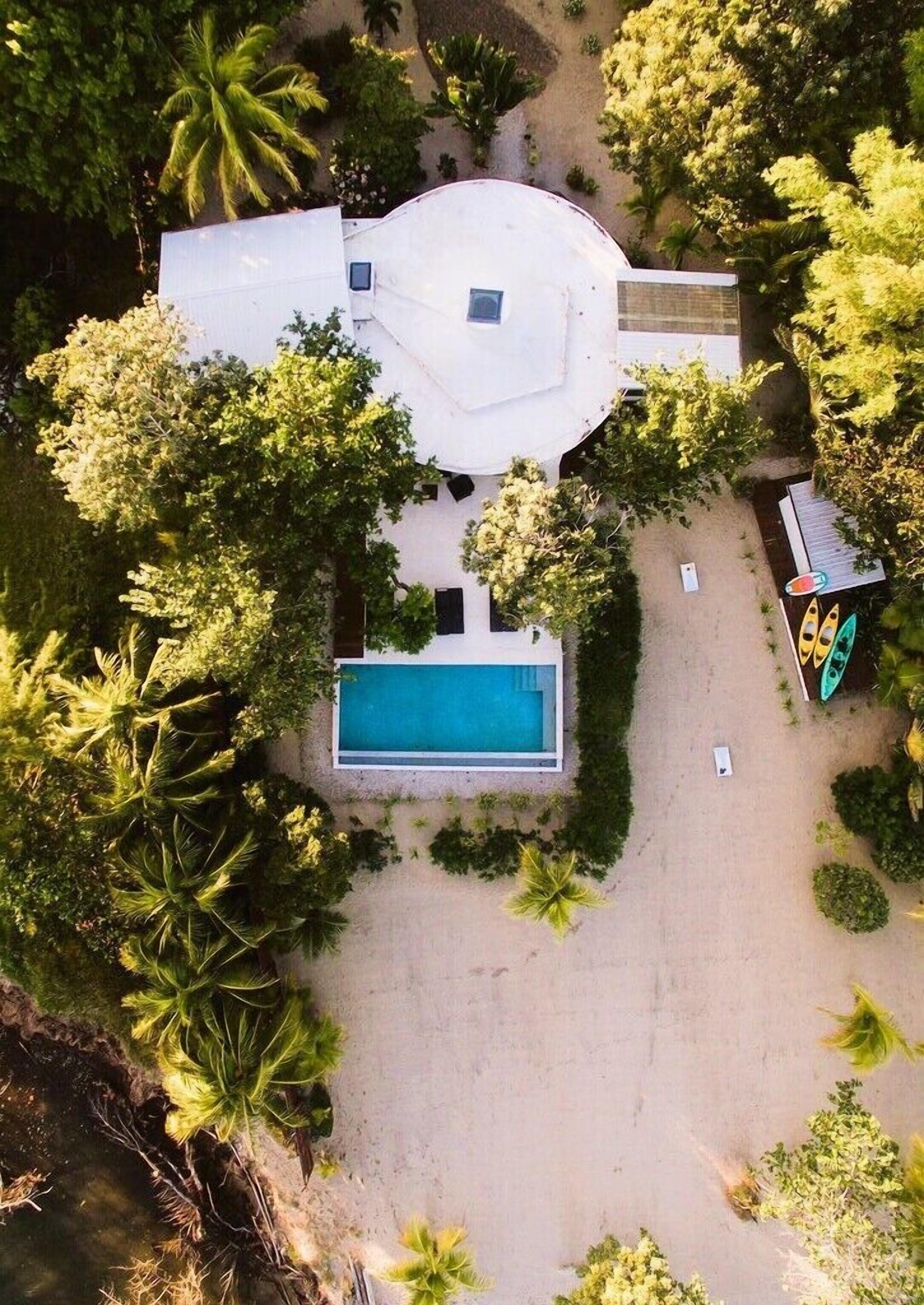 Une vue aérienne d’une maison avec une piscine, entourée d’une végétation luxuriante et de palmiers.