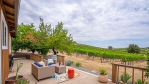 A patio with outdoor furniture, a view of a vineyard, and a wooden deck railing.