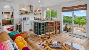 A modern kitchen with a central island, a dining area with chairs, and a large window with a vineyard view.