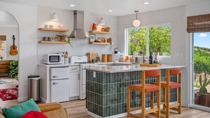 A modern kitchen with a central island, white cabinetry, and a large window offering a view of greenery.