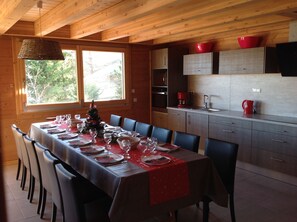 Een eetruimte met een lange tafel gedekt voor een maaltijd, houten wanden en een raam met uitzicht op bomen.