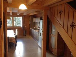 Een houten interieur met een keukenhoek, een eettafel met stoelen en een trap.