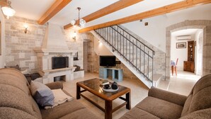 Ein gemütliches Wohnzimmer mit Kamin, Holzbalken, einer Treppe und einem Fernseher.