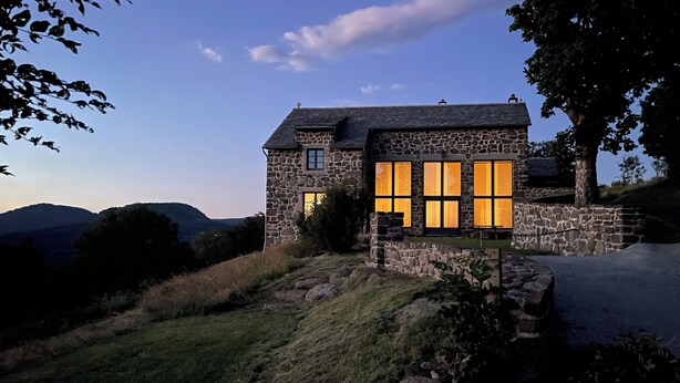 Une maison en pierre dotée de grandes fenêtres et d’une façade en pierre.