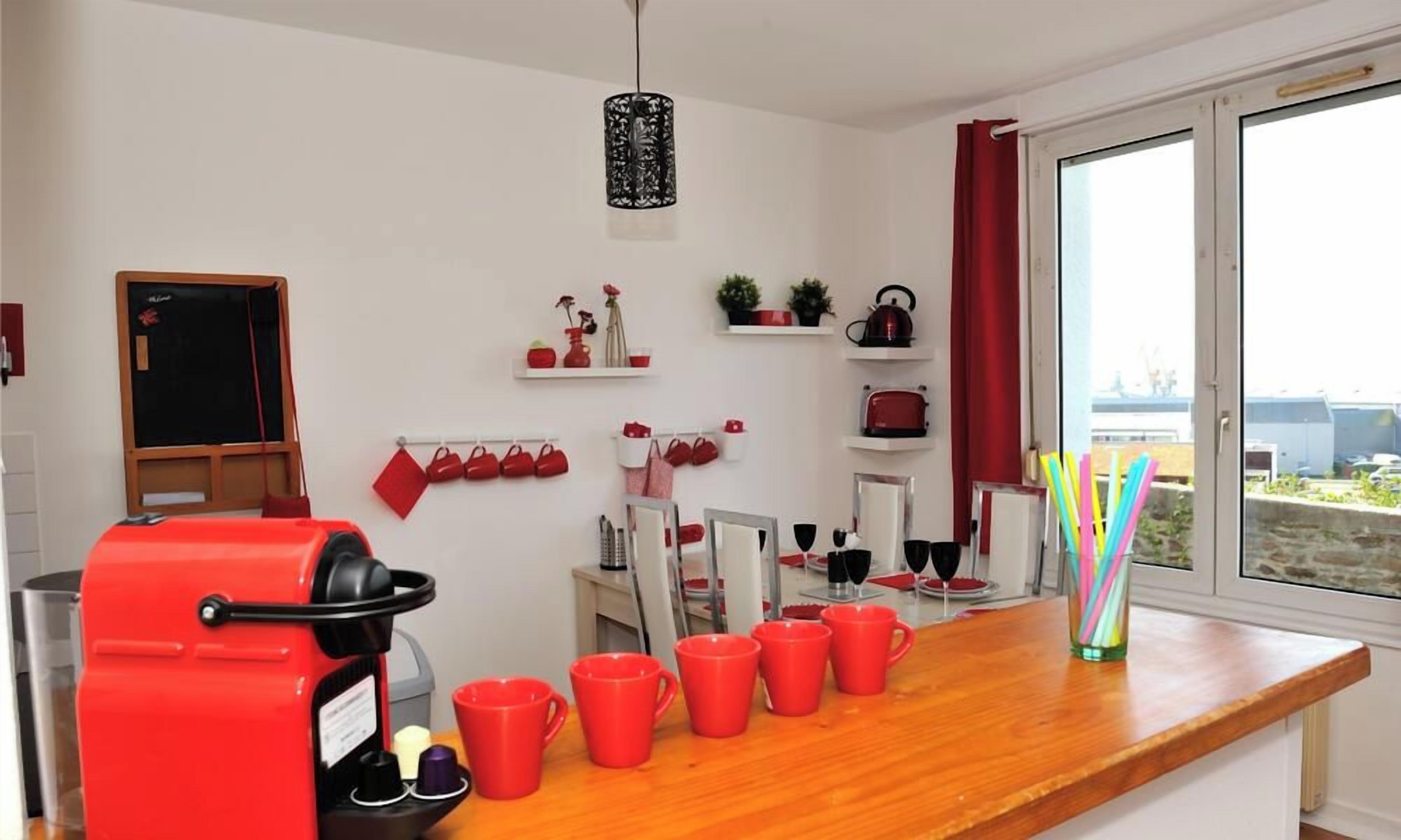 Een moderne keuken met een rode koffiemachine, meerdere rode mokken, en een raam met uitzicht op het buiten.