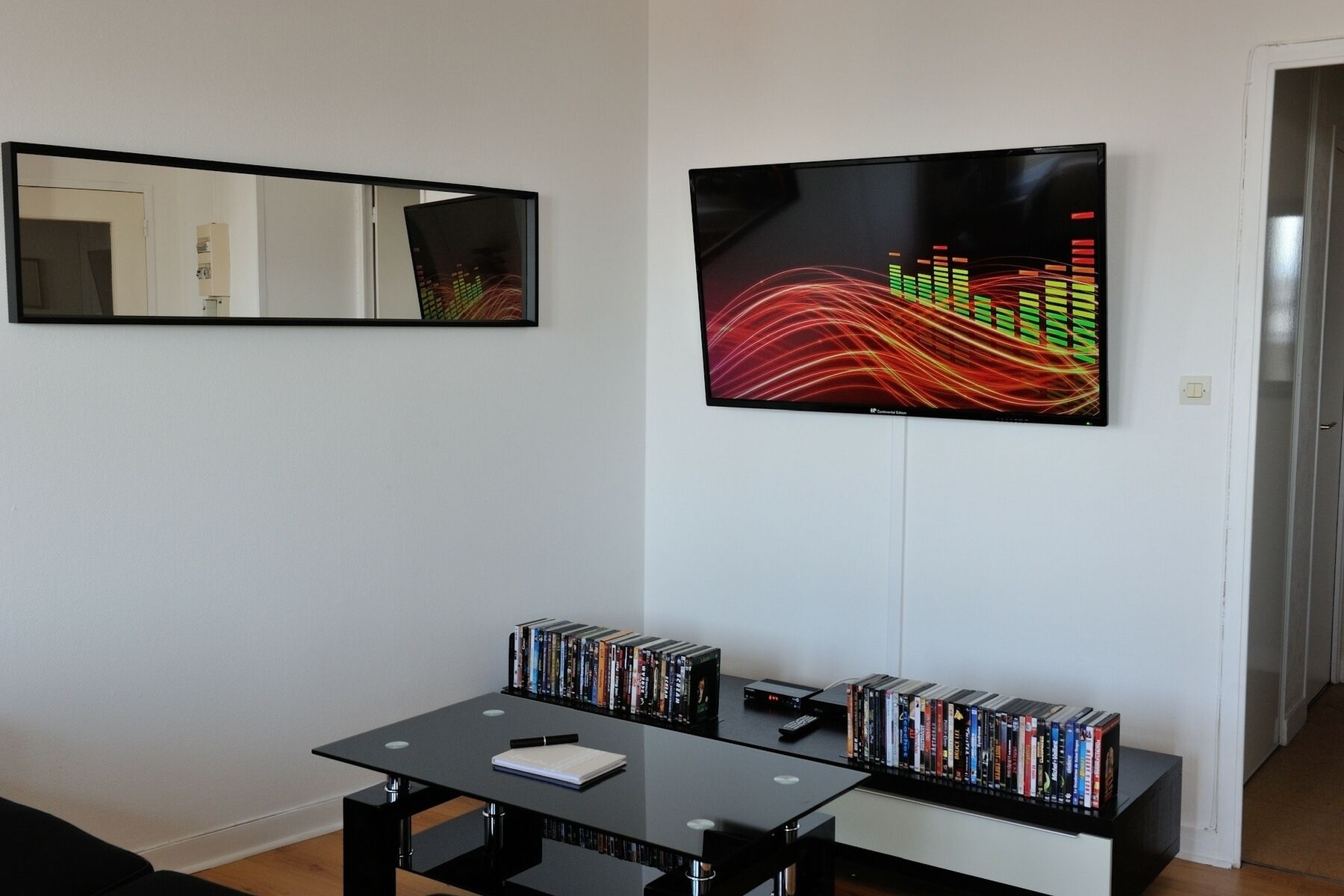 En moderne stue med et sort bord, en reol fyldt med DVD'er og et stort abstrakt billede på væggen.