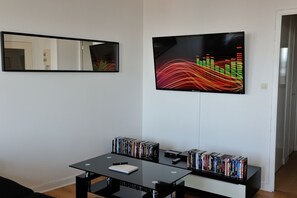 A modern living room with a black table, a bookshelf filled with DVDs, and a large abstract painting on the wall. - Appart Cosy Brest vue mer (Brest)