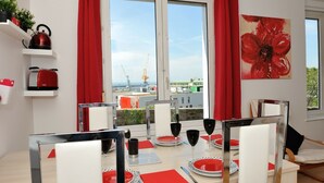 Un comedor con una mesa dispuesta para cuatro personas, platos rojos y blancos, copas de vino negras y una tetera roja sobre un estante blanco.