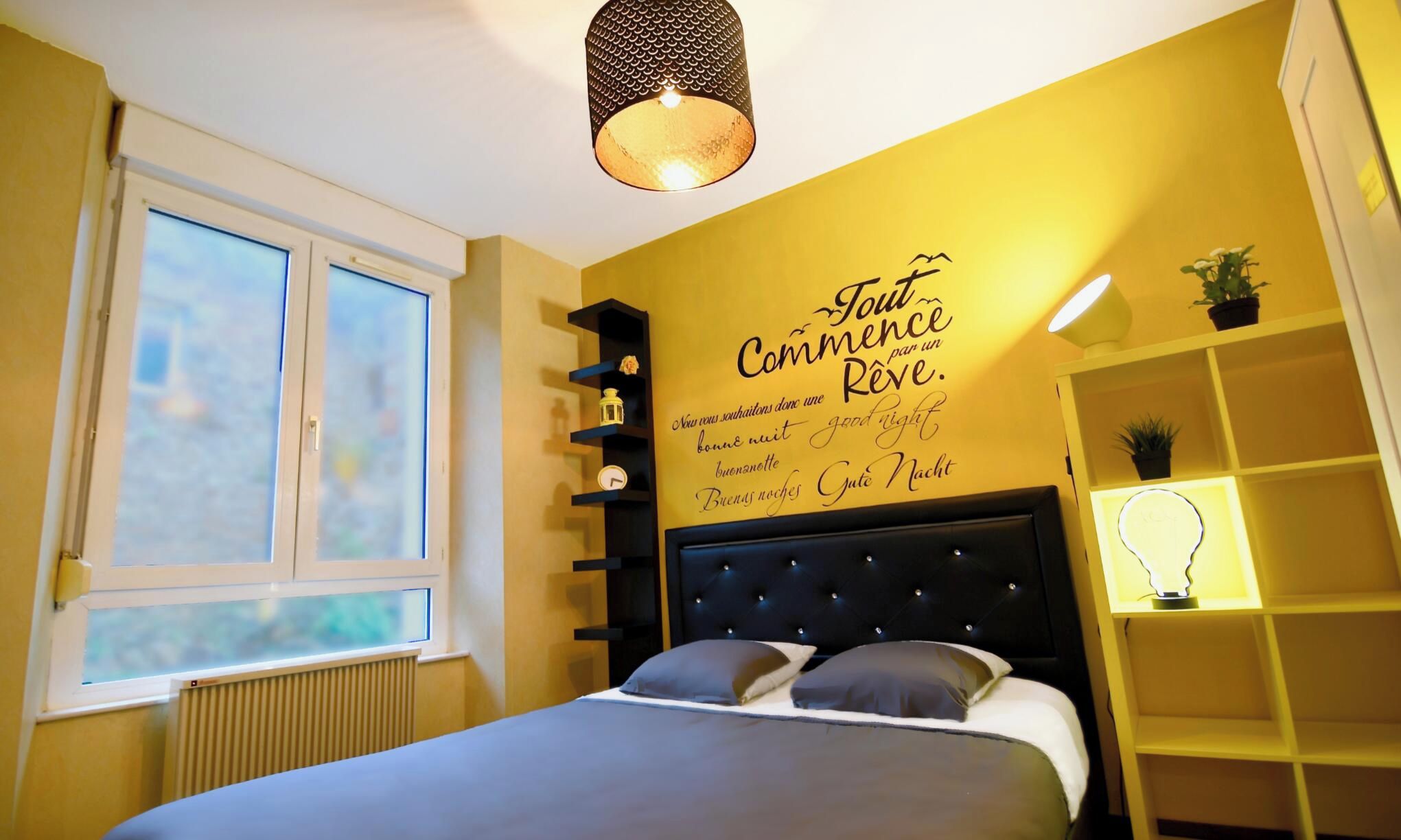 Un dormitorio con una cama, una ventana, una pared con una cita y una estantería con plantas.