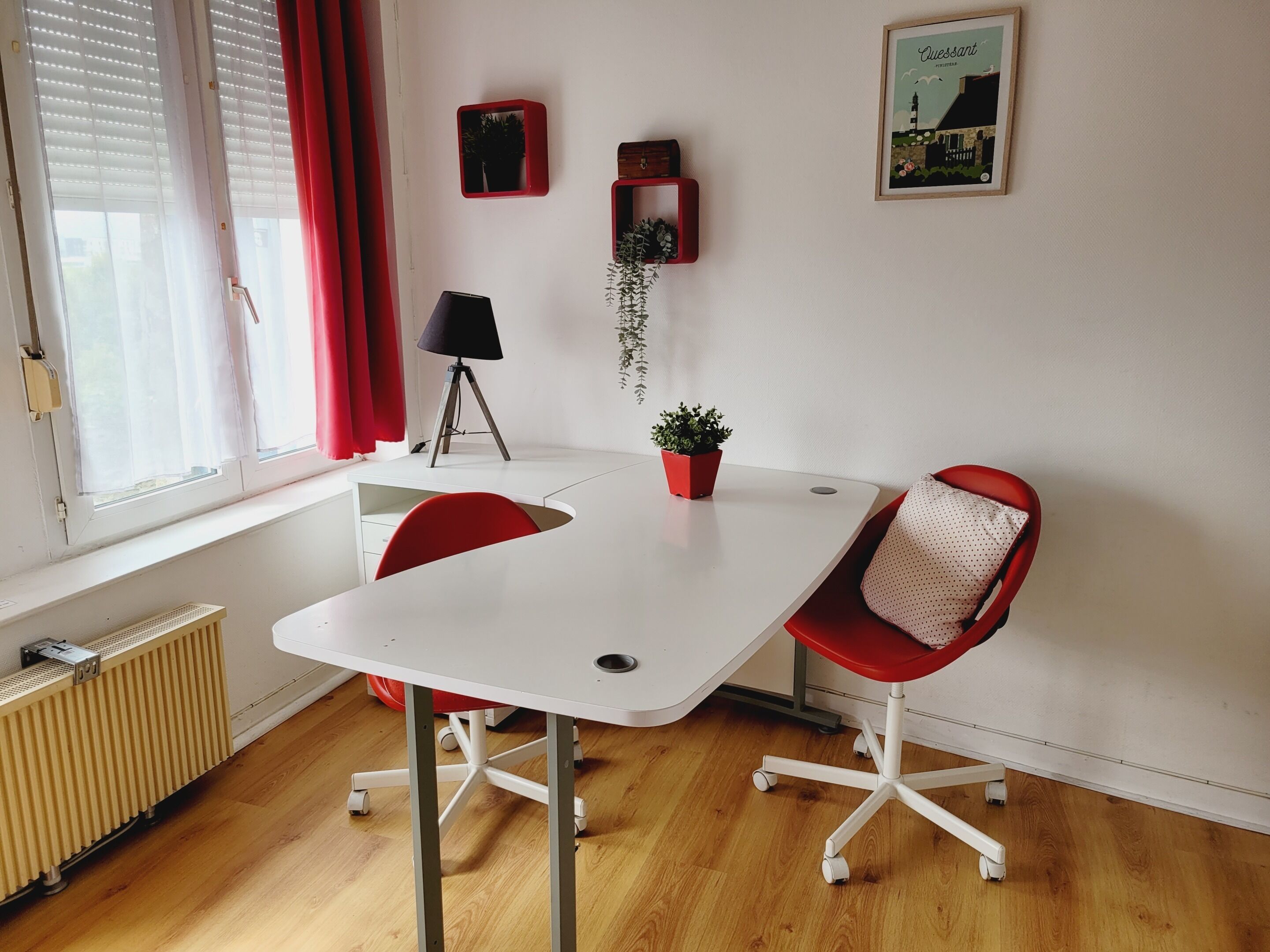 A room with a white table, red chairs, a radiator, a lamp, and a framed picture on the wall.