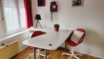 A room with a white table, red chairs, a radiator, a lamp, and a framed picture on the wall.