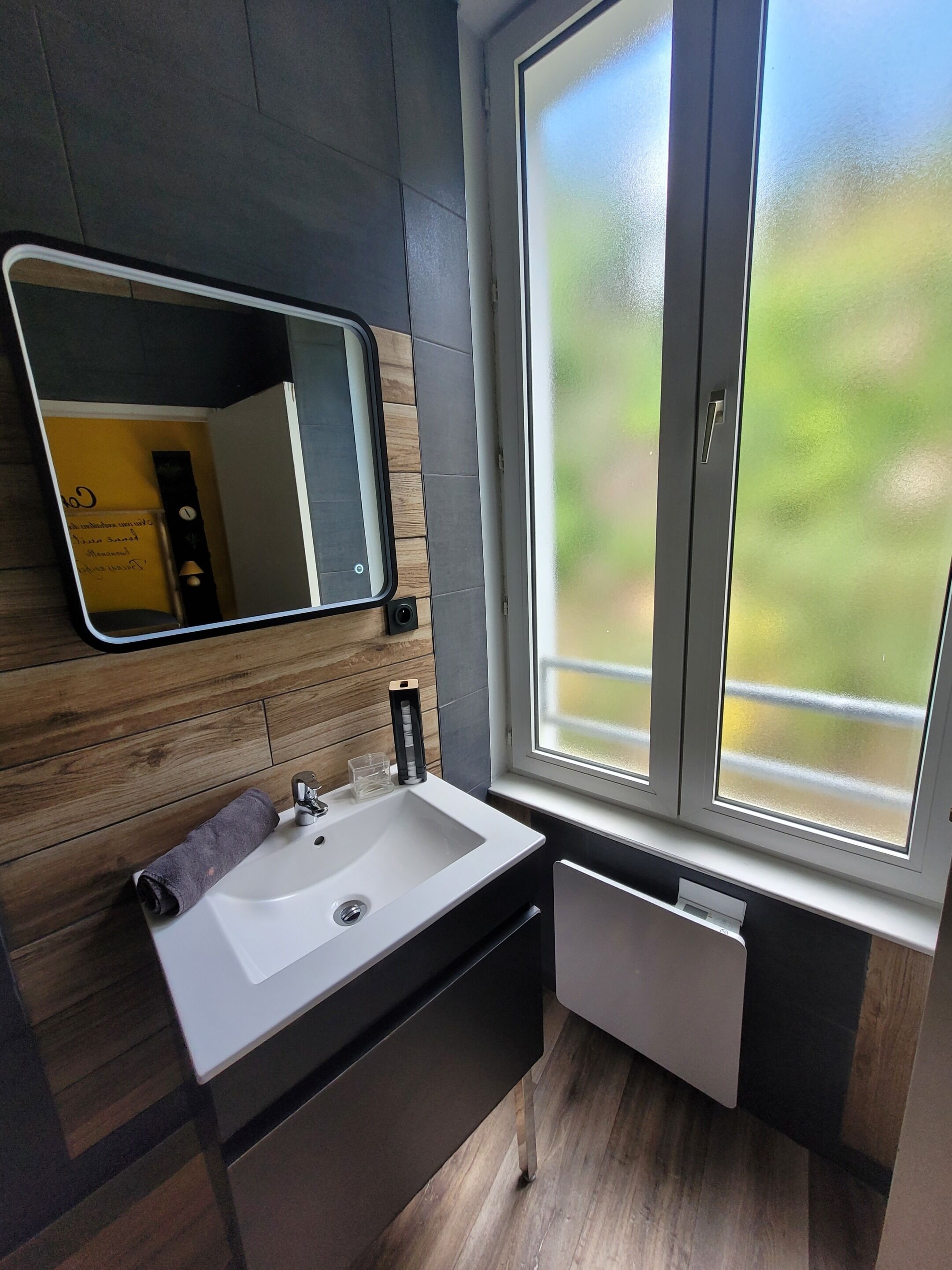 Un baño moderno con un lavamanos blanco, un espejo y una ventana con vidrio esmerilado.