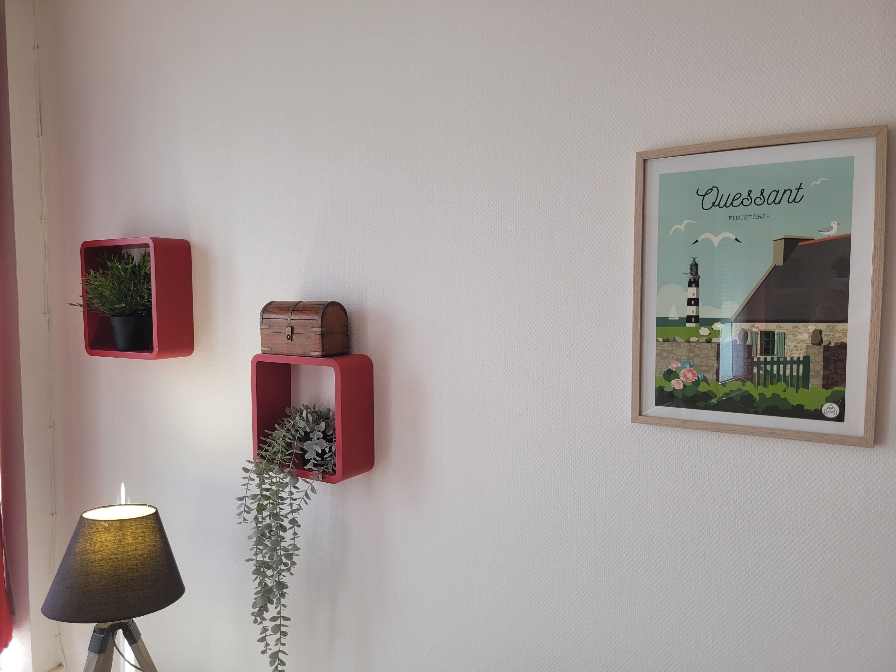 A wall with three red storage boxes, a framed illustration, and a lamp.