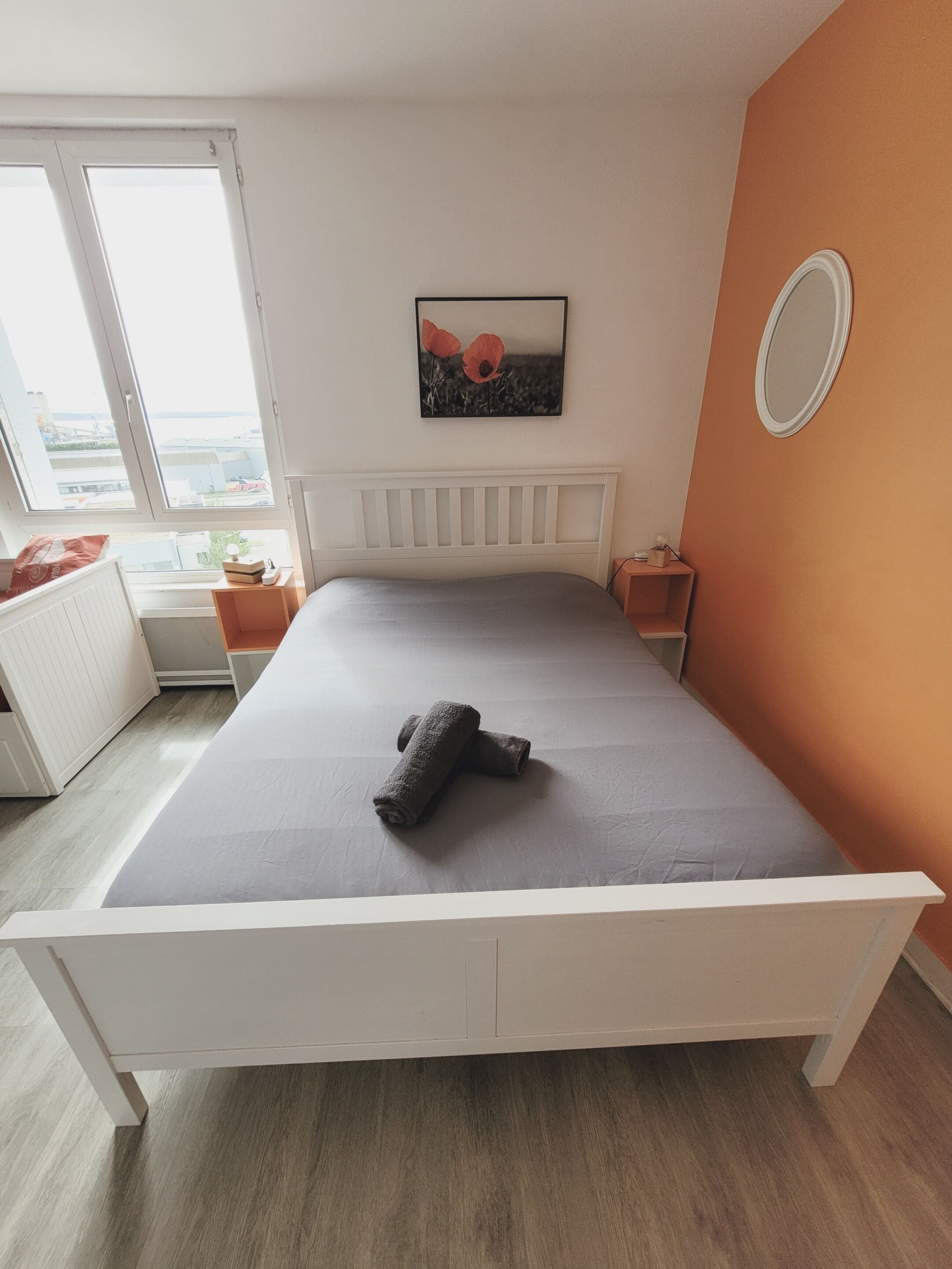 Un dormitorio con una cama, una ventana, un cuadro y un espejo.
