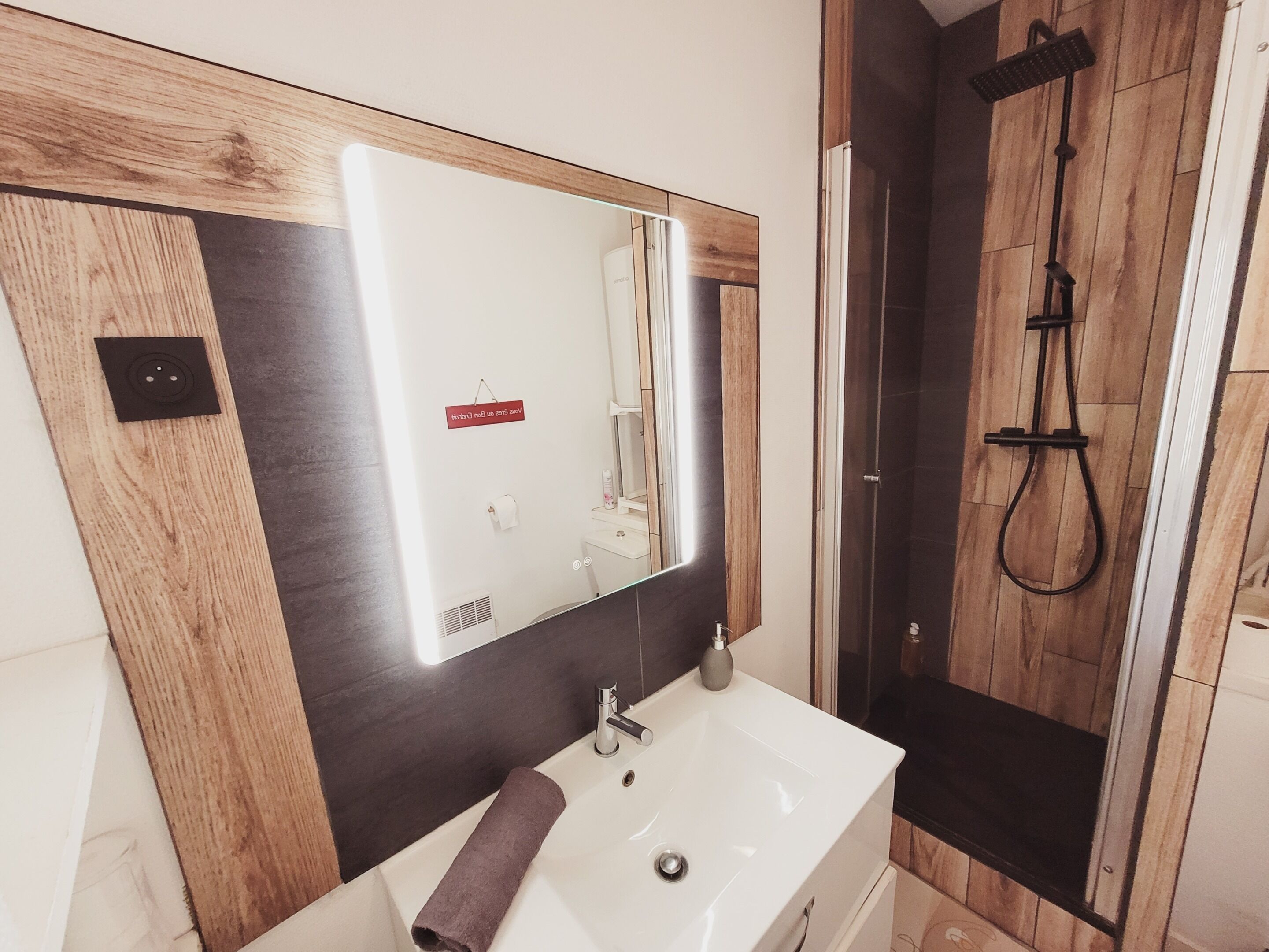 Une salle de bain avec un meuble-lavabo en bois, un lavabo blanc, un miroir et un espace douche.