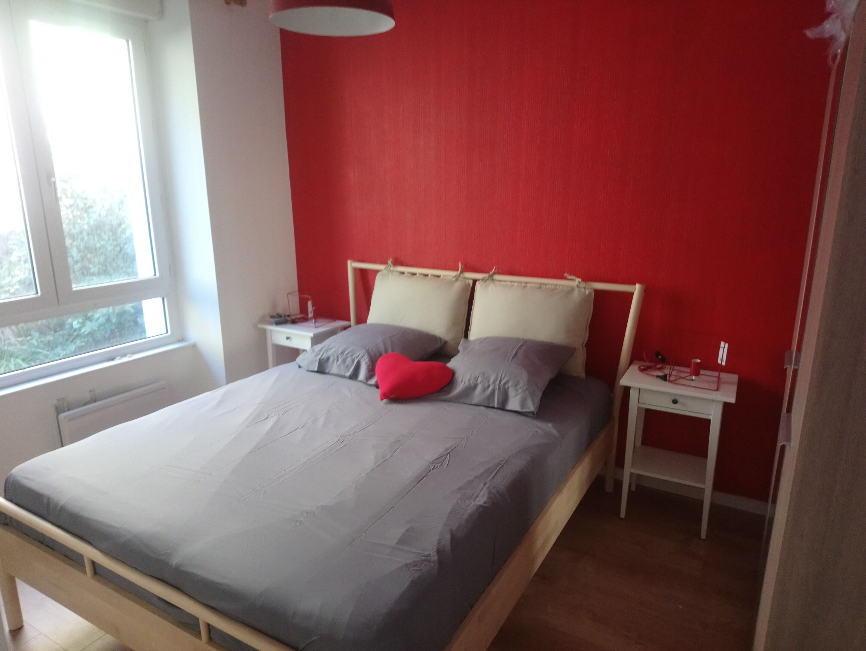 A bedroom with a bed, two bedside tables, a window, and a red wall.