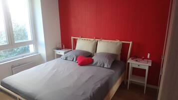 A bedroom with a bed, two bedside tables, a window, and a red wall.