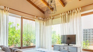 Une chambre avec un plafond en bois, un lit agrémenté d’un coussin à motifs, une télévision posée sur une commode et une fenêtre avec des rideaux.