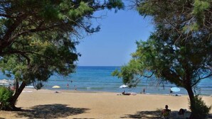 Une plage avec des arbres, des parasols et des gens.